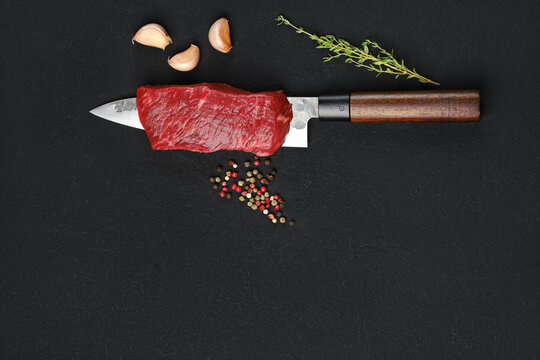 Piece of raw beef steak on the blade of knife