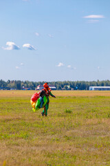 A woman skydiver walks across the field with a parachute.