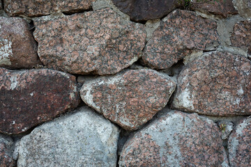 Ancient stone wall. Weathered rough surface of old masonry. Granite rock. Wall of a medieval castle. Vintage texture great for background and design.