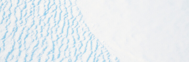 Wide panoramic winter background with snowy ground. Natural snow texture. Wind sculpted patterns on snow surface.