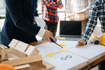 Three colleagues discussing data working and tablet, laptop with on on architectural project at construction site at desk in office..