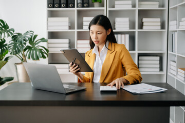 Asian businesswoman working in the modern office with working notepad, tablet and laptop documents