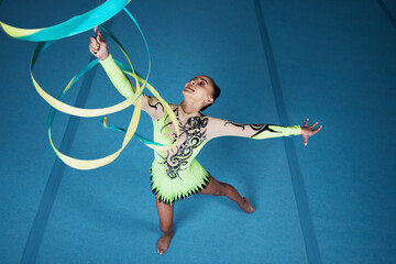 Dance, rhythmic gymnastics and woman in gym with ribbon in air, action with performance top view and fitness. Competition, athlete and female gymnast, creativity and art, routine and energy at arena - obrazy, fototapety, plakaty