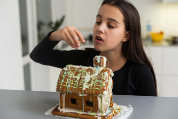 A teenage girl is eating a gingerbread house