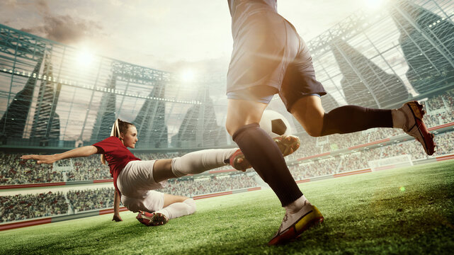 Dynamic image of female football players in motion during match, game. Woman hitting ball and falling down. 3d arena, blurred audience. Concept of professional sport, competition, dynamics, game, ad