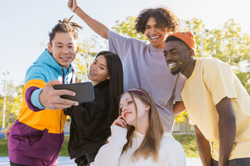 Multiracial group of young friends bonding outdoors and taking a selfie with smartphone for social...