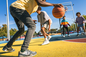 Multiracial group of young friends bonding outdoors and having fun playing a basketball match at...