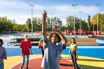Multiracial group of young friends bonding outdoors and having fun playing a basketball match at...