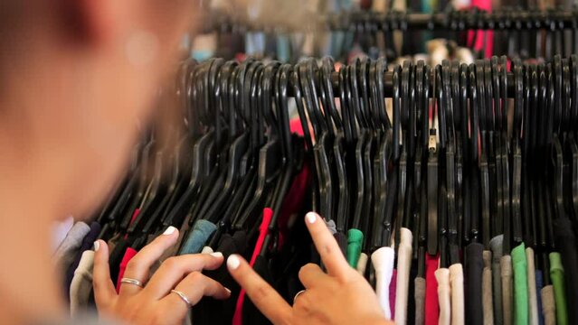 Young woman choosing t-shirt from hanger in second hand clothing store, 4K consumerism reduse reuse recycle concept footage. Chiang Mai, Thailand.