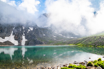 Mountain lake and rocky mountains. Crystal clear lake in the middle of the rocks. Green fields, lake and mountain ranges under snow