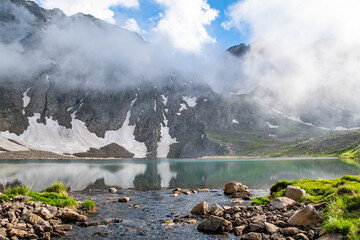 Mountain lake and rocky mountains. Crystal clear lake in the middle of the rocks. Green fields, lake and mountain ranges under snow