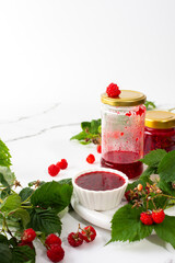 Homemade summer preservation, raspberries jam in jars, jars with jam and raspberry sprigs