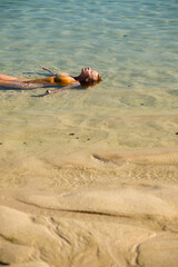 Obraz premium A young, sexy girl of European appearance, in a yellow bathing suit, lies in the sea, blue water on the beach, relaxes and sunbathes.