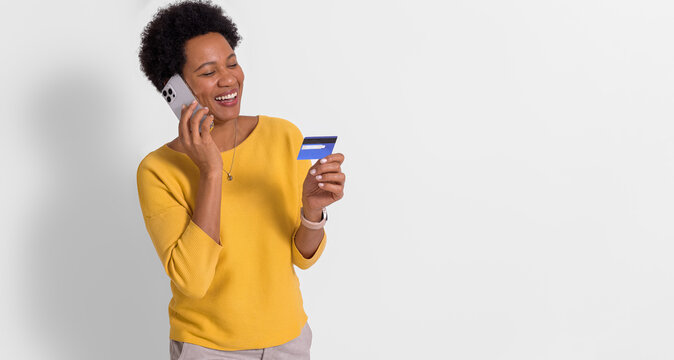 Happy Woman With Afro Hair Talking Over Smart Phone And Looking At Credit Card On White Background