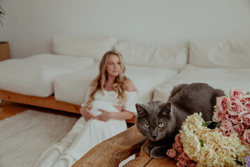 Cat sitting on a table with flowers and a pregnant girl in the background