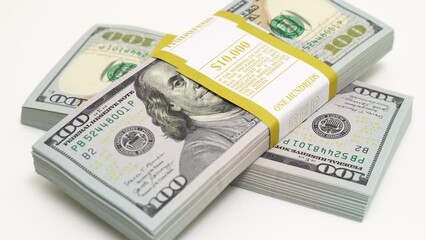 stack of bank bundles with US dollars on a white background. Close-up shot of new, freshly printed hundred-dollar bills rotating on a table. cash flow, business investment, or big money concepts. - Powered by Adobe
