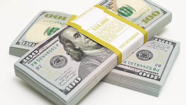 stack of bank bundles with US dollars on a white background. Close-up shot of new, freshly printed hundred-dollar bills rotating on a table. cash flow, business investment, or big money concepts.