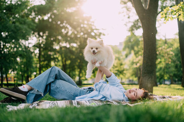 A young woman lies on the grass and holds her Pomeranian dog in her arms.