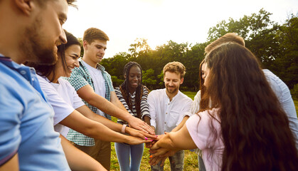 Multiracial men and women outdoors in summer. Group of cheerful young friends stacking their hands together while having fun in park. Human relationship, social, community and team building concept.