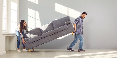 Happy couple placing sofa in living room of new home. Smiling husband and wife carrying couch in...