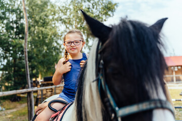 Portrait of little cute girl with two braids walking with a pony in manege at open air outdoor....