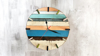 Wooden wall clock with a round dial and arrows, different colors on a plastered concrete wall