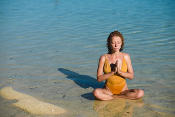 A young girl, with blond hair, of European appearance in a yellow swimsuit, practices yoga, and...