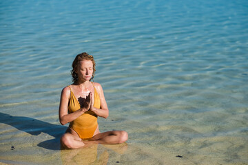 A young girl, with blond hair, of European appearance in a yellow swimsuit, practices yoga, and...