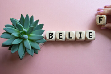 Belief symbol. Concept word Belief on wooden cubes. Businessman hand. Beautiful pink background...
