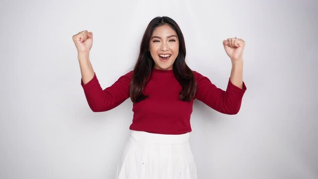 A young Asian woman with a happy successful expression wearing red top isolated by white background