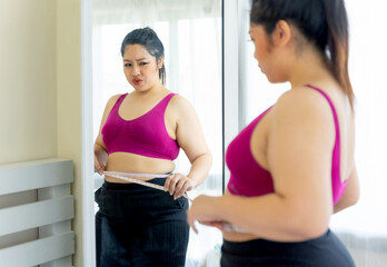 Fototapeta na wymiar asian fat women , Fat girl , Chubby, overweight plus size looking the mirror measuring her waist in the bedroom - lifestyle Woman diet weight loss overweight problem concept