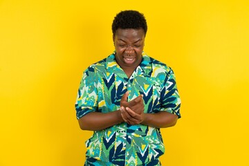 Young latin man wearing hawaiian shirt over yellow background Suffering pain on hands and fingers,...