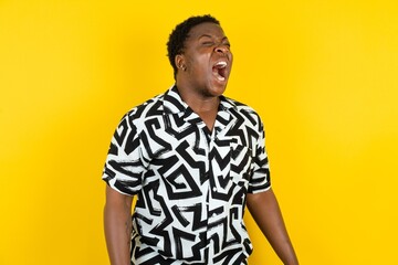 Young latin man wearing printed shirt over yellow background angry and mad screaming frustrated and furious, shouting with anger. Rage and aggressive concept.