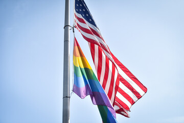 LGBTQIA flag and United States of America flags seen together hoisted on a pole