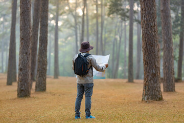 Asian naturalist looking at the map for direction while exploring wildlife in the pine forest for...