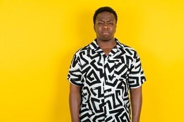 Dismal gloomy rejected Young latin man wearing printed shirt over yellow background has problems...