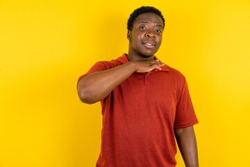 Young latin man wearing red t-shirt over yellow background cutting throat with hand as knife,...