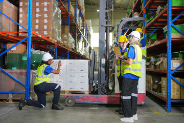 Worker working in large warehouse holding paper chart check list checking the material compare with the boxes wrapped with plastic keep on wooden pallet ready to ship to customer