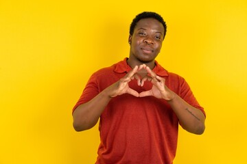 Serious Young latin man wearing red t-shirt over yellow background keeps hands crossed stands in thoughtful pose concentrated somewhere