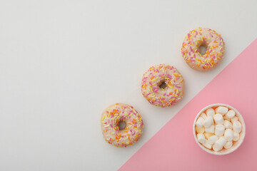 Donuts and paper cup with marshmallows on pink and white background, space for text