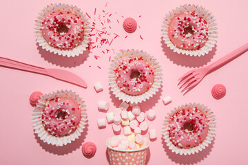Donuts, paper cups with marshmallows and cutlery on pink background, top view