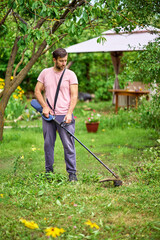 Young man cutting grass with weed cutter on his grassy lawn.