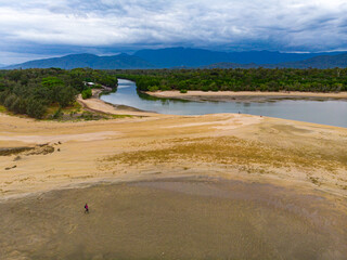 lonely girl walking on the sandy beach near the mouth of river in balgal beach, north queensland, australia