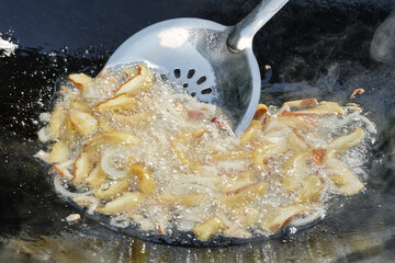 Sliced Porcini mushrooms and onions in boiling oil on frying pan with metallic kitchen spatula. Preparing food outdoors. Shallow depth of field