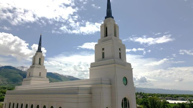 Smooth drone shot of the Layton LDS Mormon Temple moving from side to the right and up seeing blue sky and Wasatch mountains in back ground.