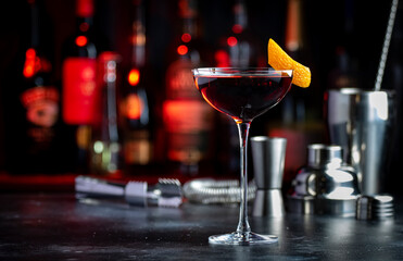 Adonis alcoholic cocktail drink with sherry and red vermouth, black bar counter background, steel tools and bottles