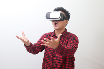 Portrait of Asian man in red plaid shirt using Virtual Reality (VR) glasses and protecting himself by spreading his arms from something big falling from above. Isolated image on white background