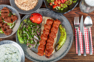 Grilled Turkish adana kebab with grilled vegetables, onion and rice on a wooden board. Dark background.