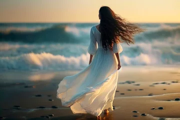 Foto op Aluminium Beautiful slim woman with long flowing brown hair in white fluttering dress in the wind against the background of the sea at sunset. Back view. Generative AI © Yaroslav