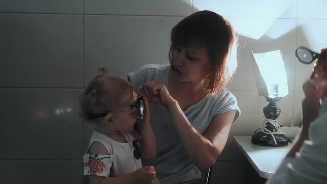 Little girl is at pediatric ophthalmologist's appointment. Optometrist puts on special medical device glasses trial lens frame to check eyesight of 2 years old female kid with eye disease, strabismus